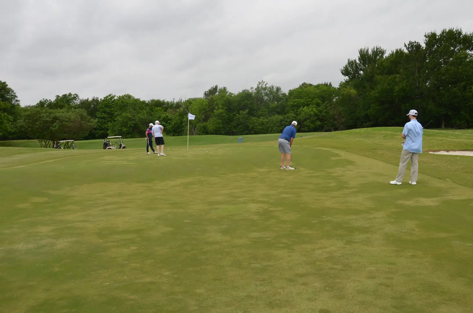 four people playing golf near the hole with a white flag