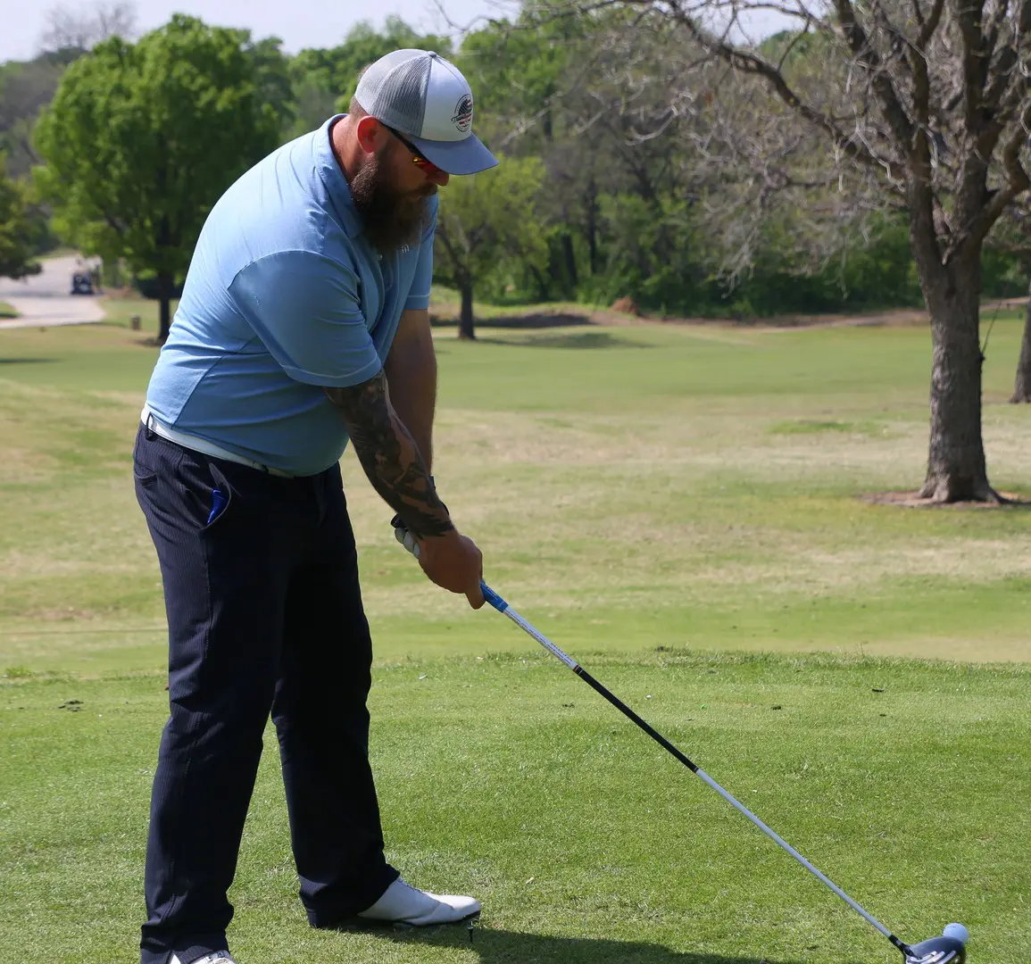 A bearded man swinging a golf club on a golf course.