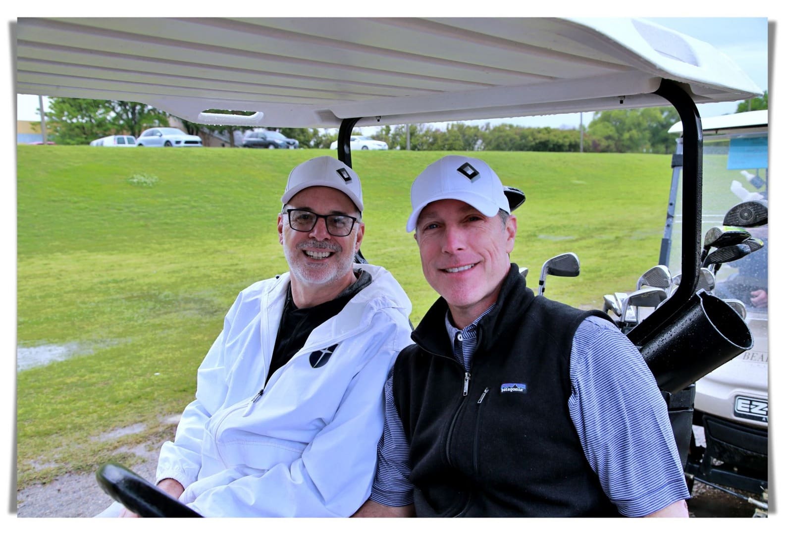 Two men smiling while sitting in a golf cart.