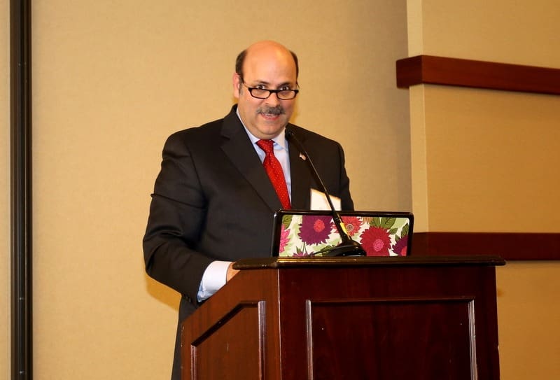 A man in a suit standing at a podium with a laptop.
