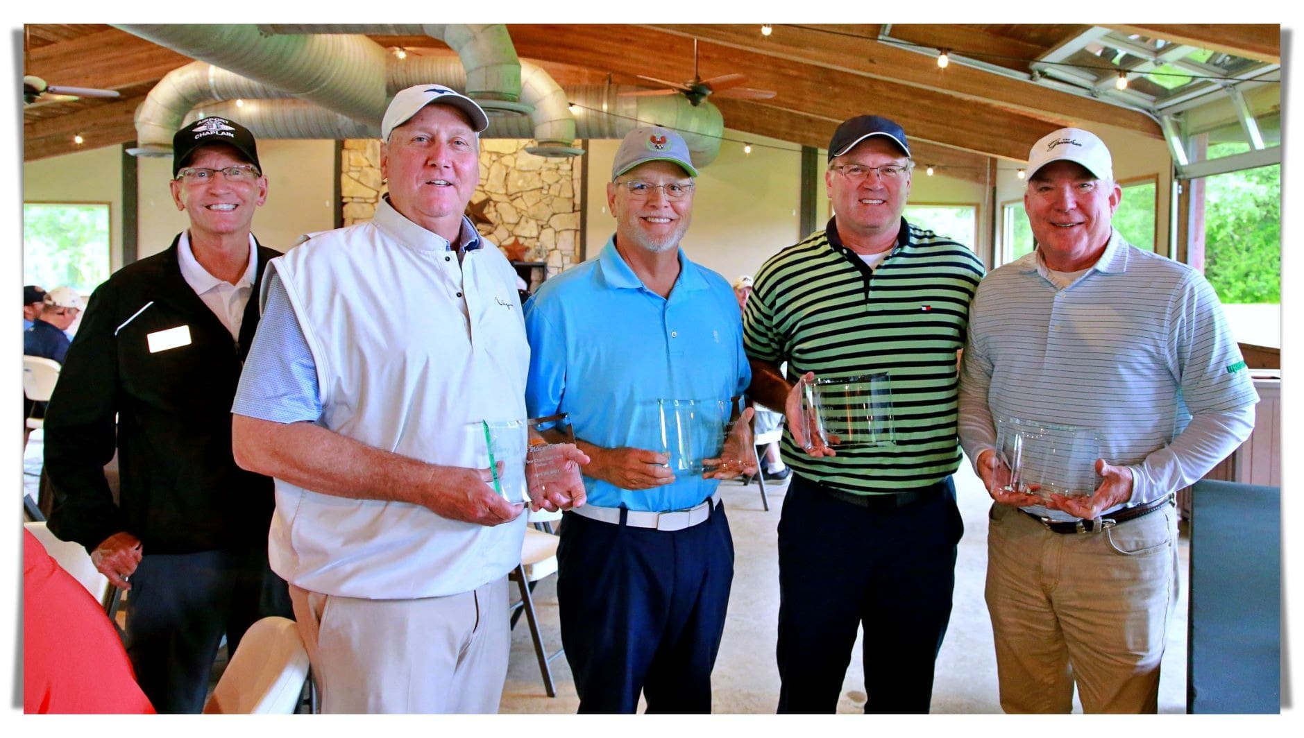 Four men holding golf trophies in front of a group of people.