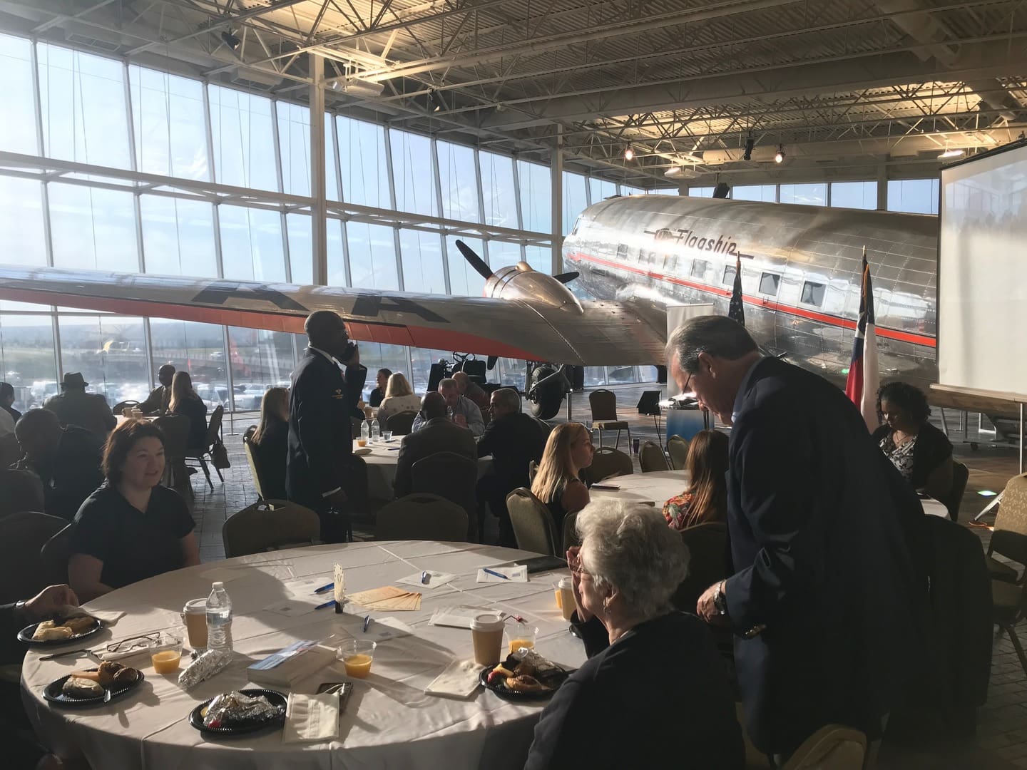 large room with windows and a plane with people eating