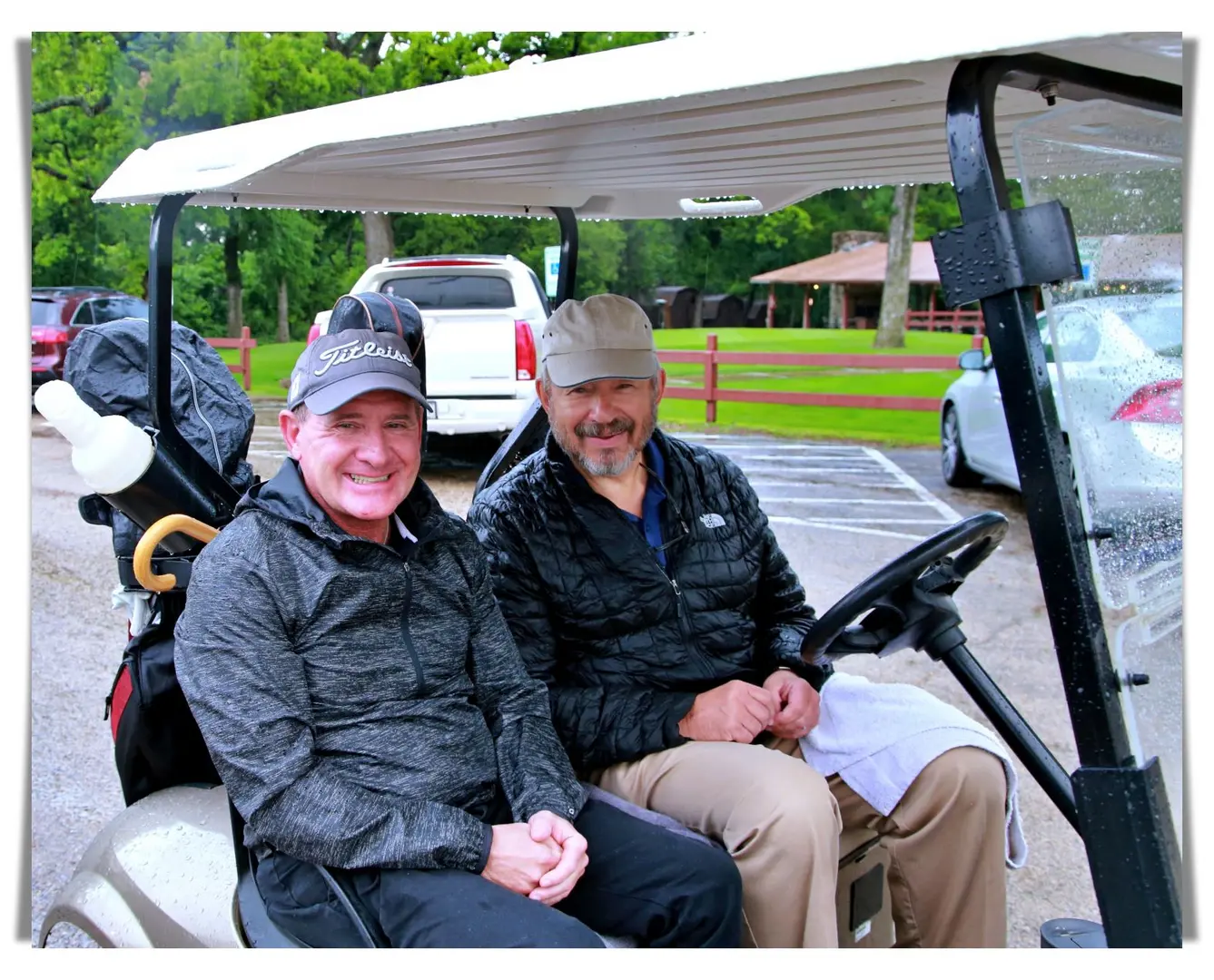 Two men sitting in a golf cart on a rainy day.